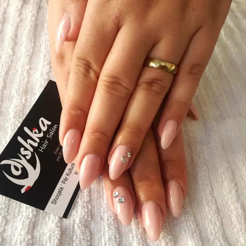 Almond-shaped nude nails with small stones, beside a Dyshka Hair Salon business card